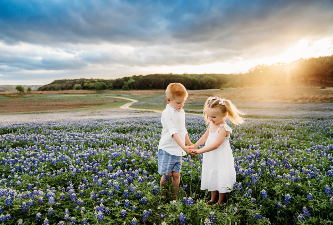 A brother and sister playing in a field of bluebonnet flowers in March.